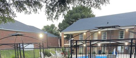 Un espacio exterior cercado con una parrilla, una piscina y un edificio al fondo.
