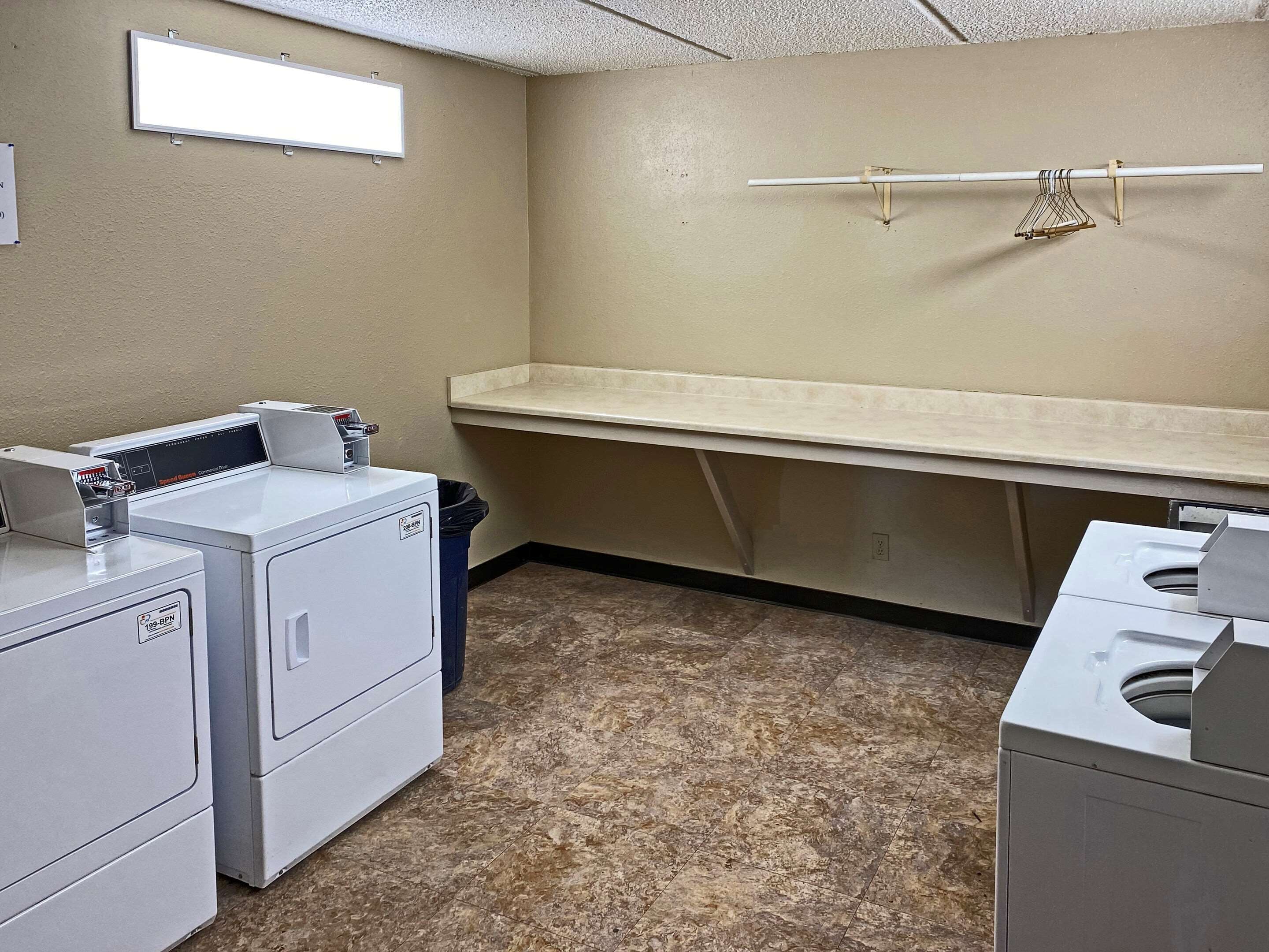 A laundry room with two front-loading washers, a dryer, a small trash bin, a window, and a towel rack.