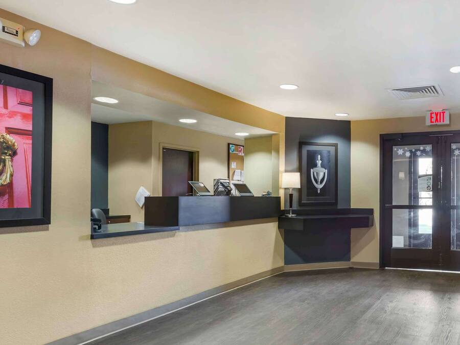 A hotel reception area with a reception desk, a framed artwork, an exit sign, and a door with frosted glass panels.