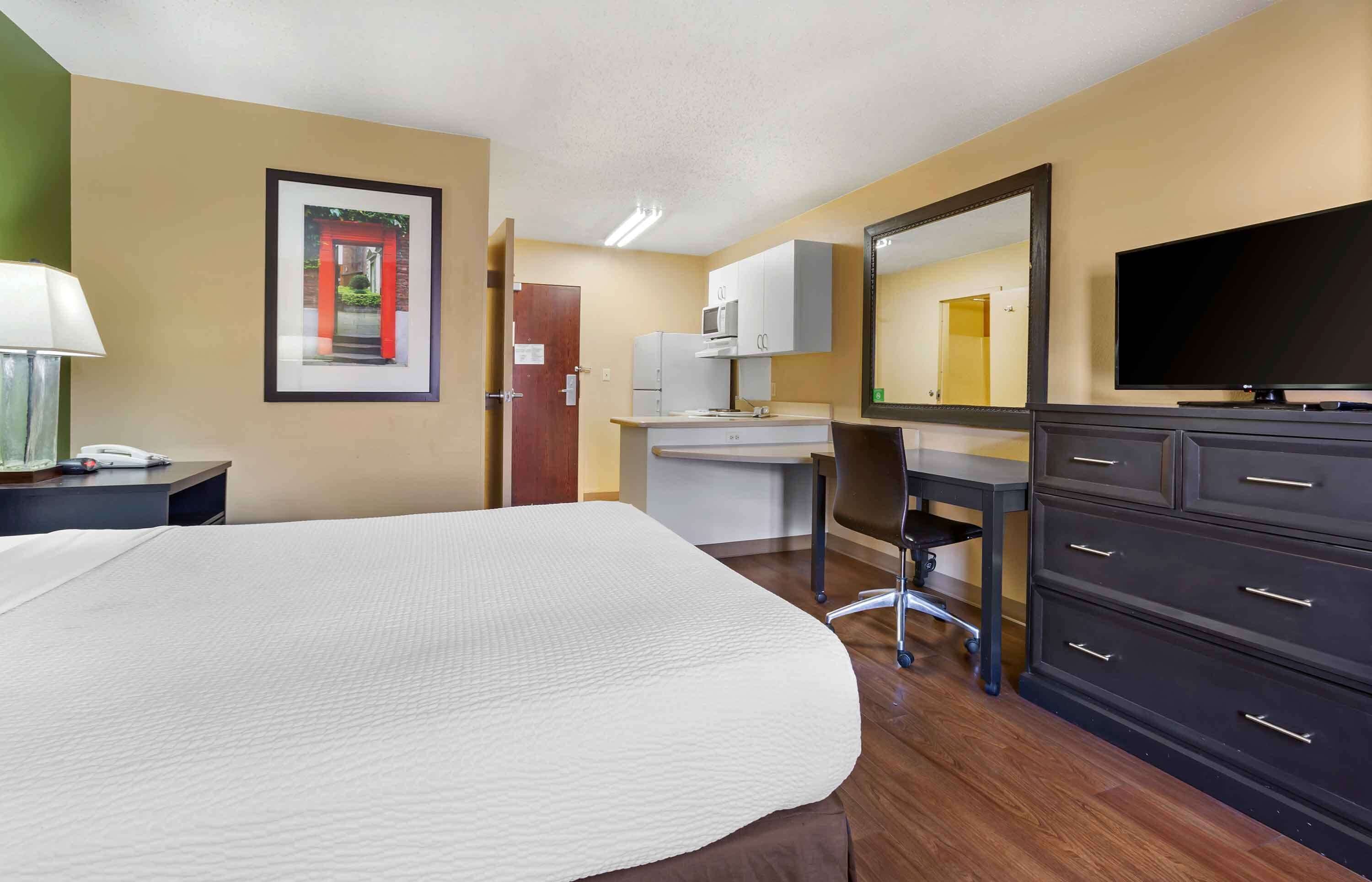 Quarto de hotel com cama, escrivaninha, cadeira, televisão, cômoda e micro-ondas.
