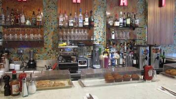 A bar area with shelves of bottles and glasses, a coffee machine, and a display case with pastries.