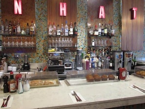 A bar area with shelves of bottles and glasses, a coffee machine, and a display case with pastries. - Hotel Newton (New York)
