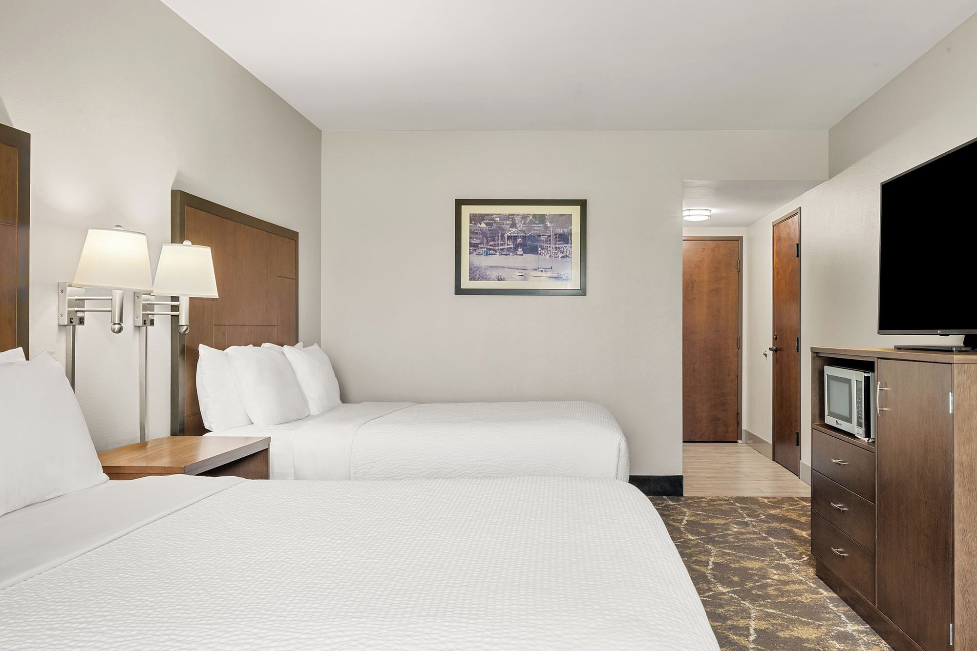 A hotel room with two beds, a TV, a desk, and a framed picture on the wall.