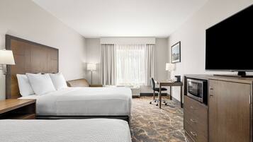 A hotel room with two beds, a desk, a television, and a minibar.
