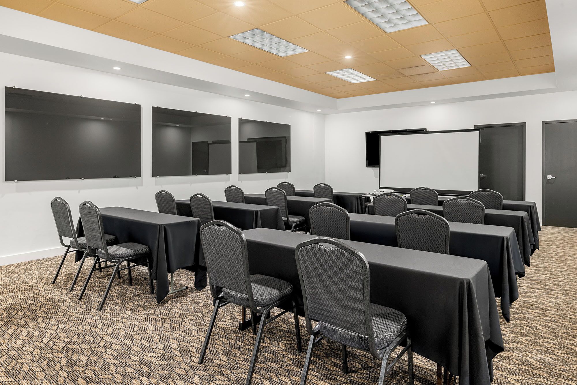 Un salón de conferencias con varias mesas y sillas, una pantalla de proyector y piso alfombrado.