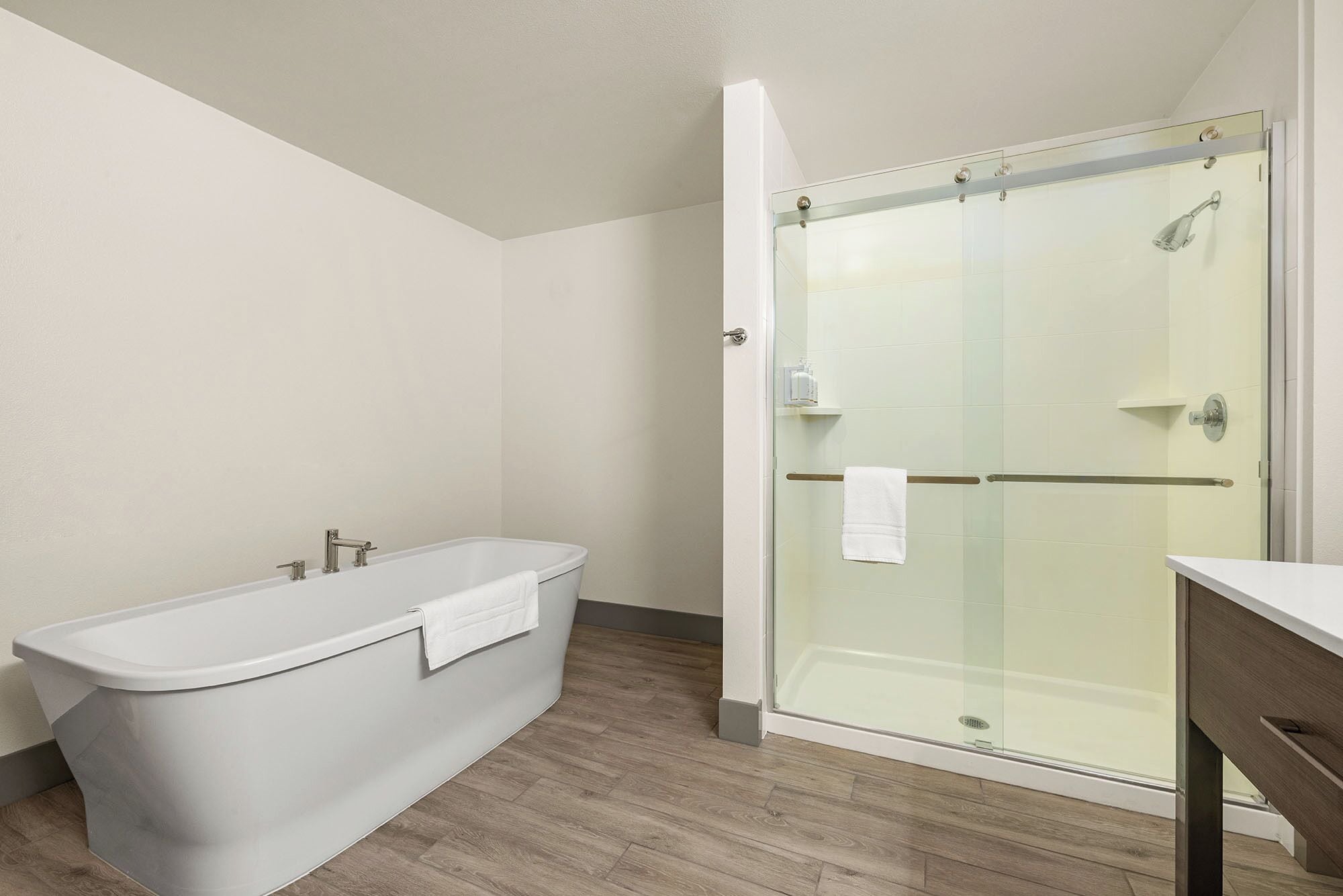 A modern bathroom with a freestanding bathtub, a glass-enclosed shower, and a wooden floor.