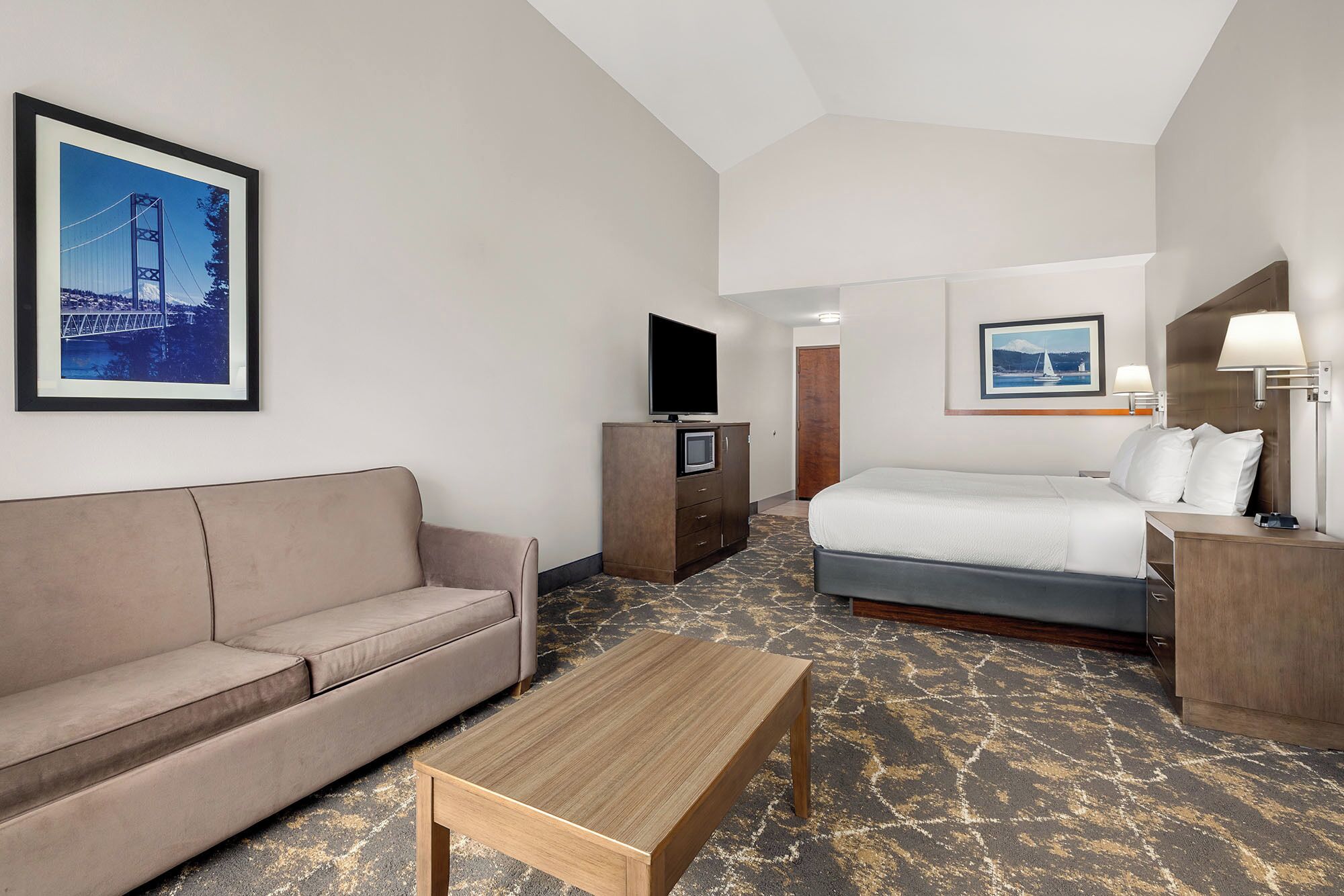 Habitación de hotel con cama, sofá, televisor, escritorio y lámpara.