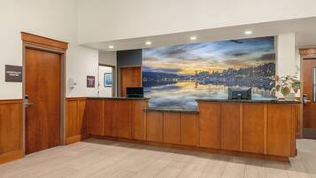 A hotel reception area with a wooden reception desk, a large scenic mural, and a sign indicating breakfast hours.