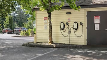 A parking area with electric vehicle charging stations, a reserved parking sign, and a building with a tree in front.