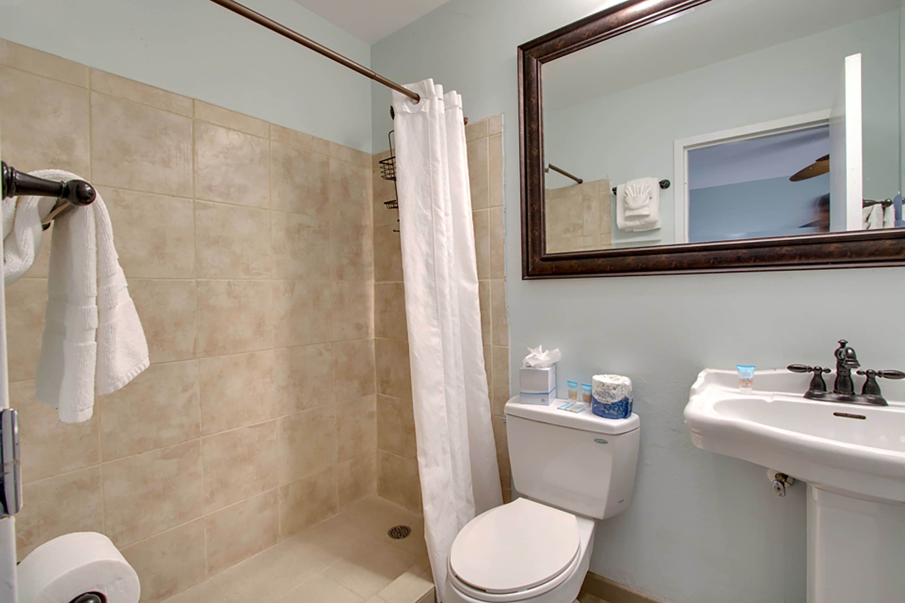 A bathroom with a shower, toilet, sink, and a mirror.