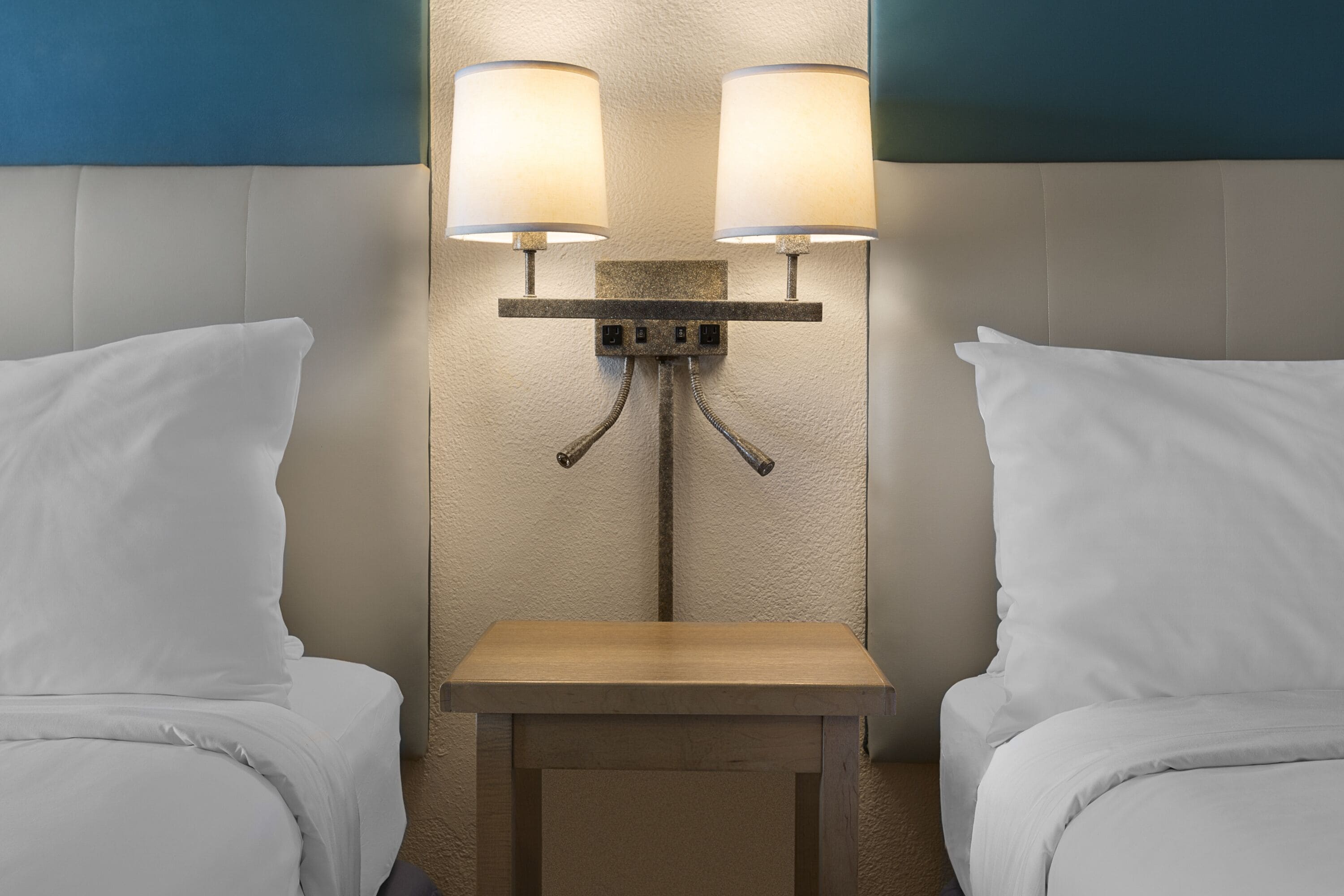 Una habitación de hotel con dos camas, una mesita de noche de madera y una lámpara fijada a la pared.