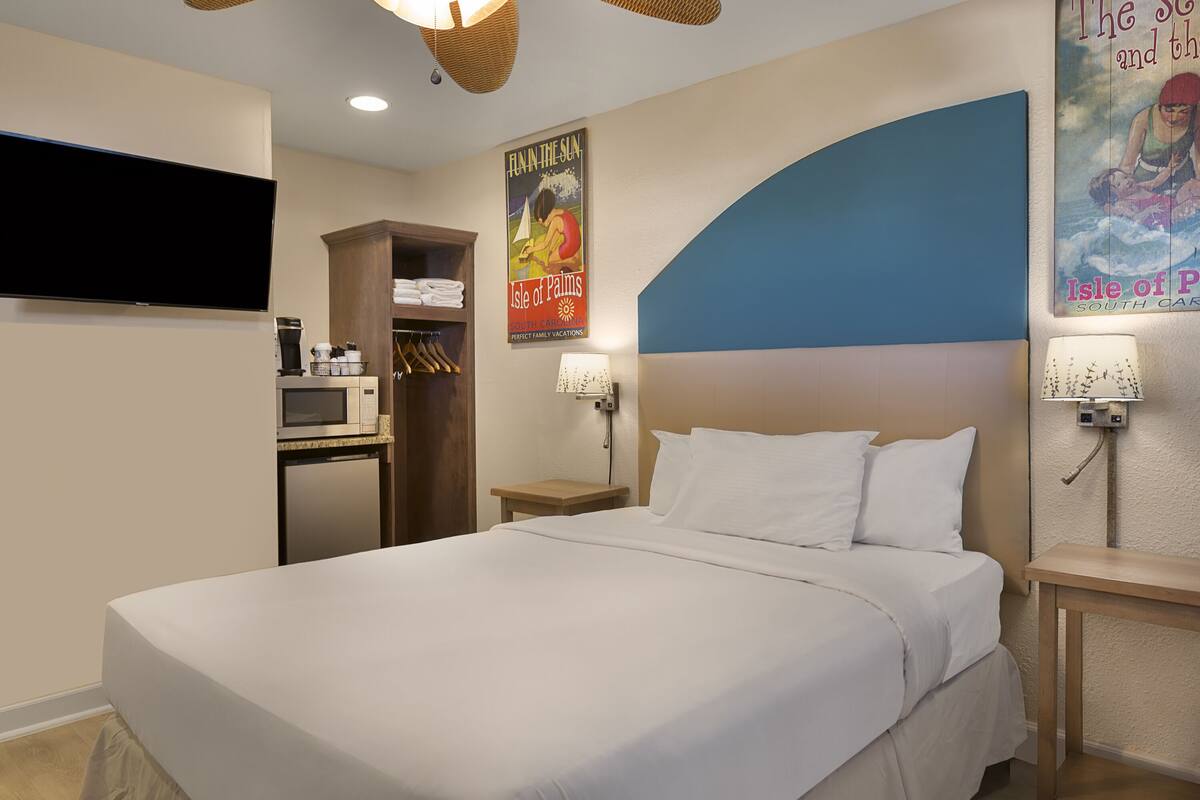 A hotel room with a large bed, a flat-screen TV, a kitchenette, and a poster of the Isle of Palm.
