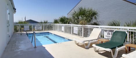 A pool area with lounge chairs, a shallow water sign, and a lifeguard duty sign.