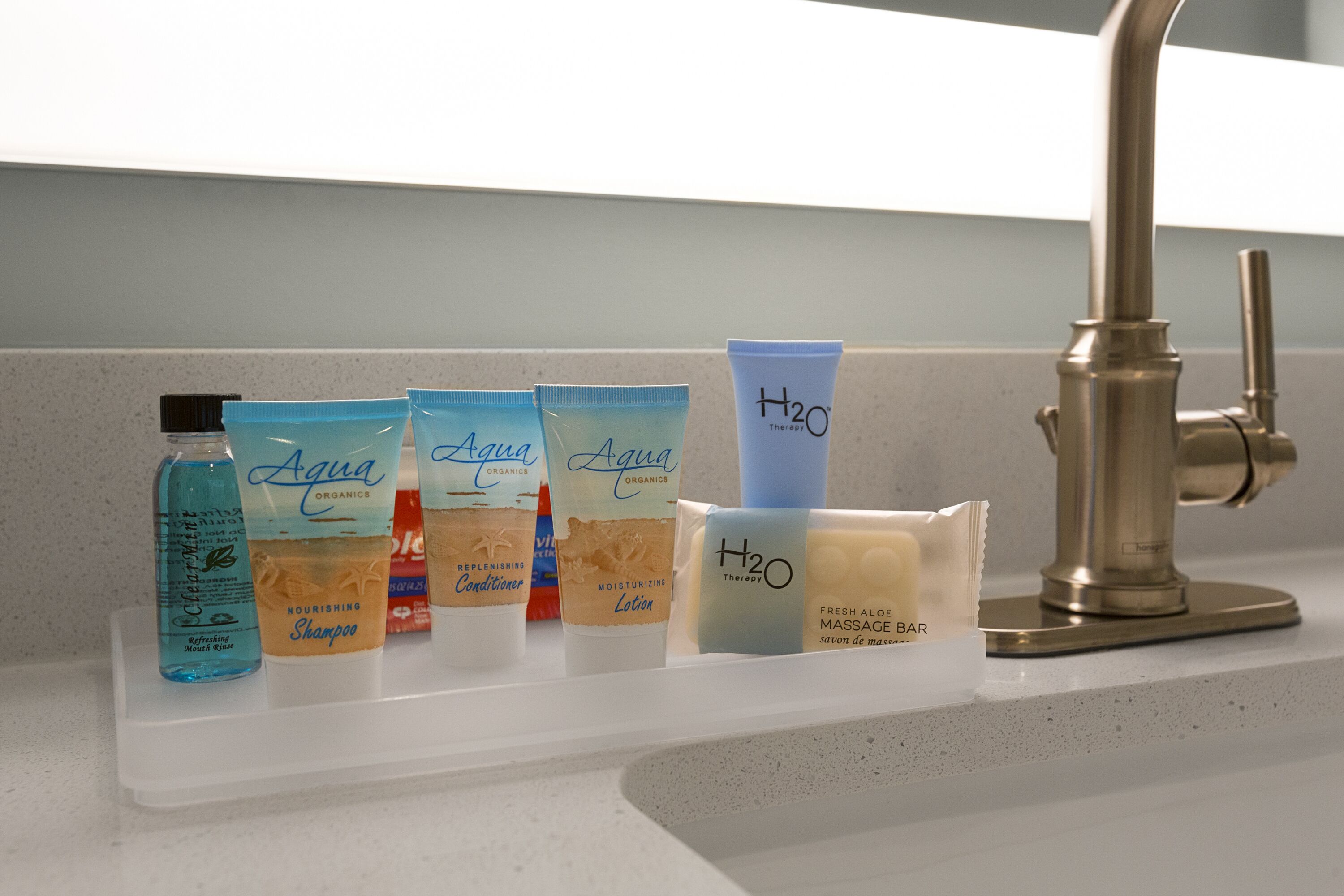 A bathroom shelf with various toiletries including a refreshing mouth rinse, nourishing shampoo, replenishing conditioner, moisturizing lotion, and a fresh aloe bar.