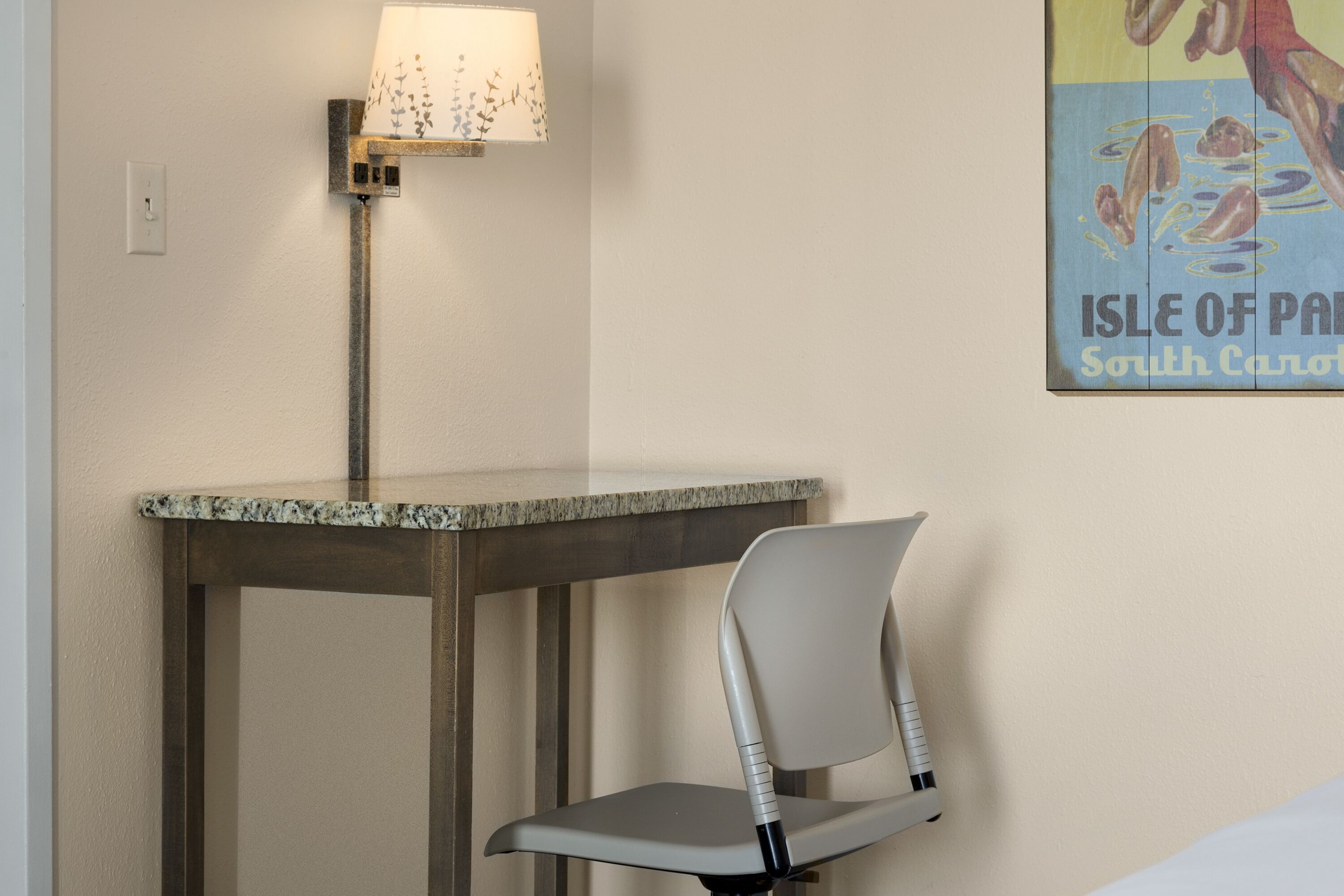 A room with a table and a chair, a lamp, and a poster on the wall.