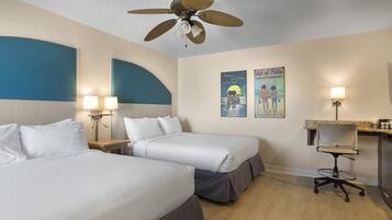 A hotel room with two beds, a desk, a chair, a ceiling fan, and wall art.