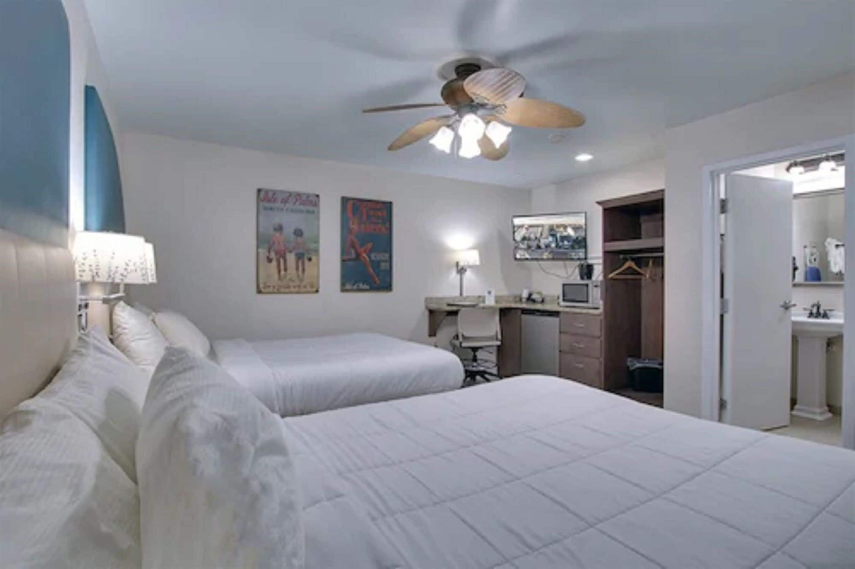 A hotel room with two beds, a desk, a computer, a wardrobe, and a bathroom.