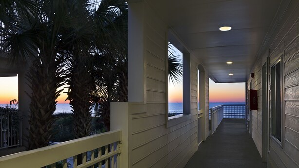 A corridor with a view of the sunset over the ocean, palm trees, and a balcony with a railing. - Seaside Inn Oceanfront (Isle of Palms)
