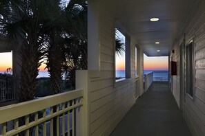 A corridor with a view of the sunset over the ocean, palm trees, and a balcony with a railing. - Seaside Inn Oceanfront (Isle of Palms)