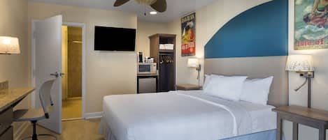 Une chambre d’hôtel équipée d’un lit, d’un bureau, d’une chaise, d’un ventilateur de plafond, d’une télévision et d’une affiche au mur.