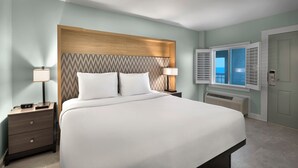 A neatly made bed with a wooden headboard, two bedside tables with lamps, a window with shutters, and a door. - Seaside Inn Oceanfront (Isle of Palms)