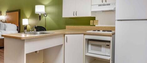 A compact hotel kitchen with a microwave, stove, and white cabinets.