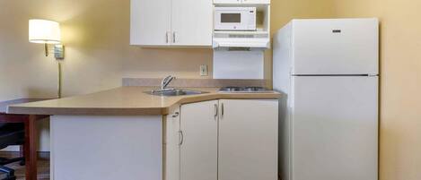 A compact kitchen with white cabinets, a built-in microwave, a refrigerator, and a sink.