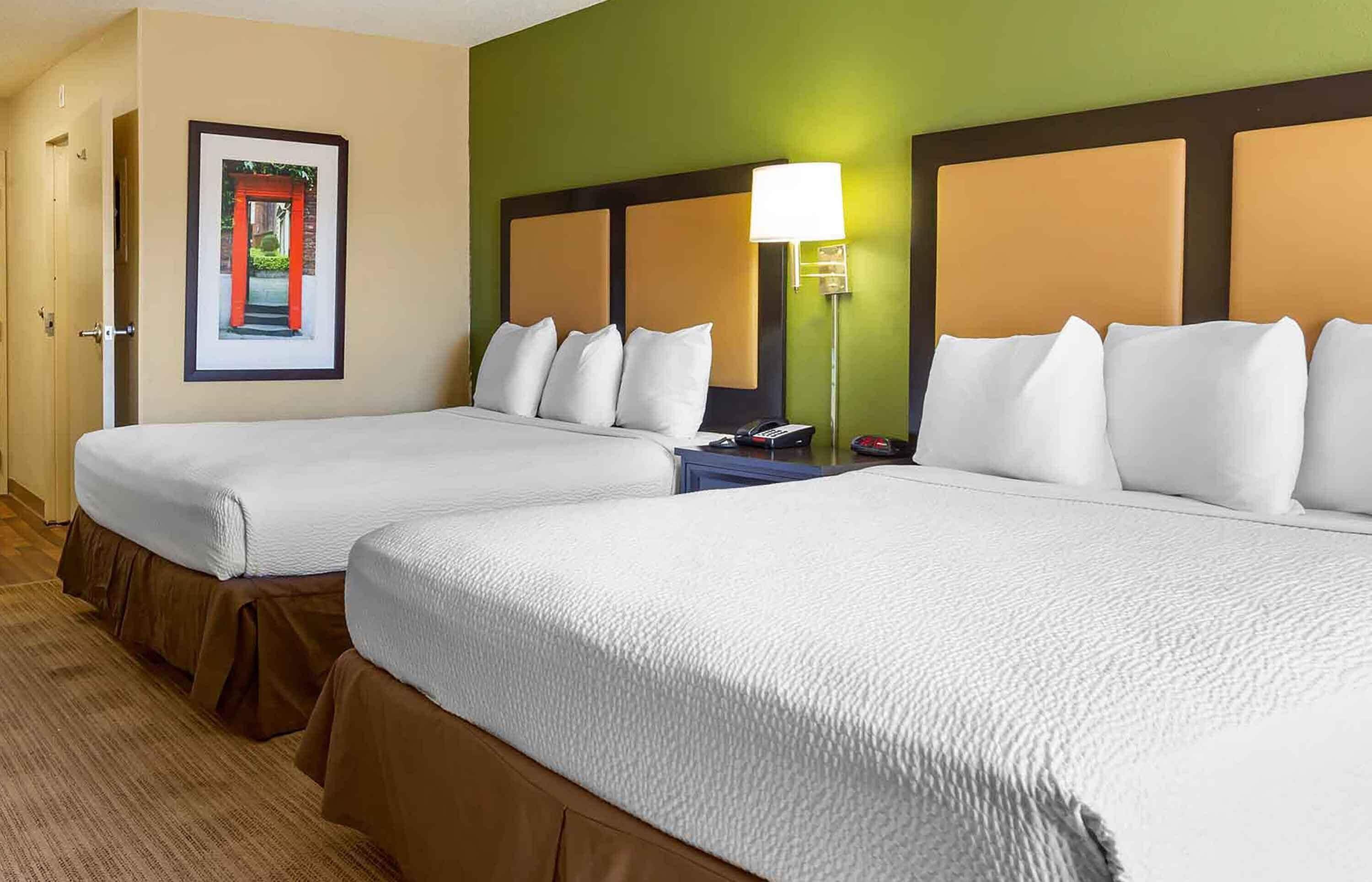 A hotel room with two beds, a framed picture on the wall, and a nightstand with a lamp.