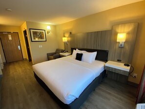 Une chambre d’hôtel avec un grand lit, des tables de chevet, une chaise et des lampes fixées au mur.
