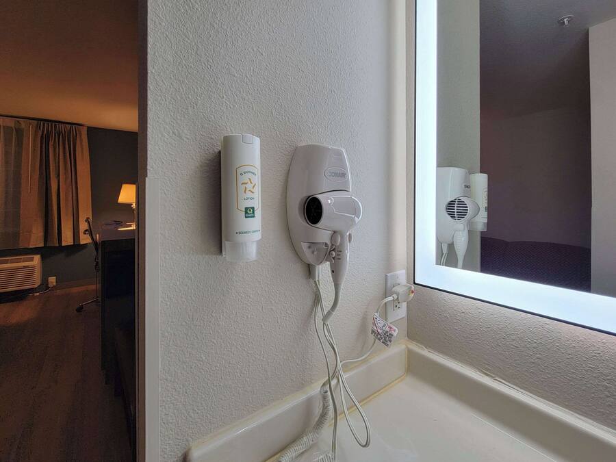 A bathroom with a hairdryer, a bottle of lotion, and a mirror.