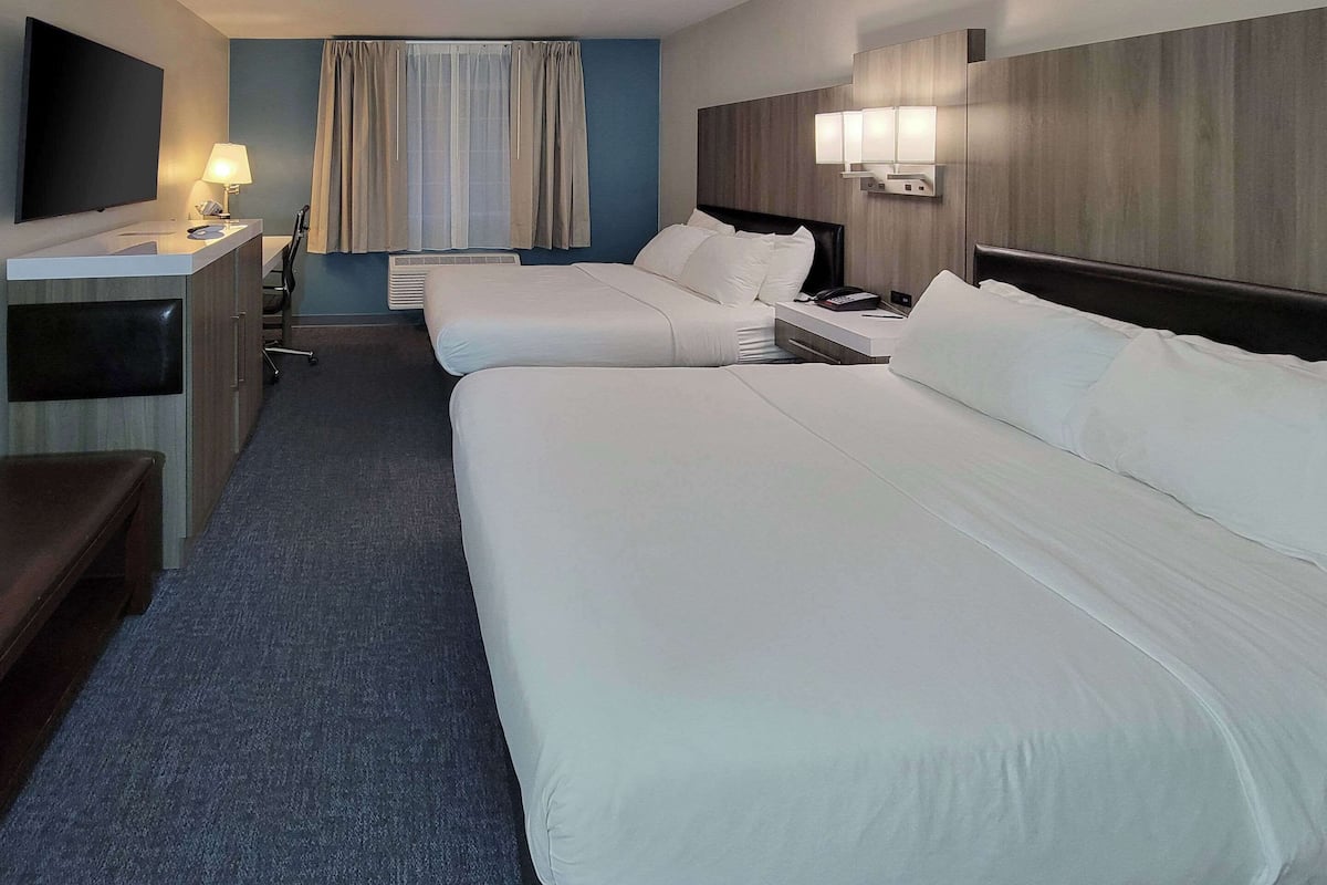 Une chambre d’hôtel avec deux lits, un bureau, une chaise, une télévision et une fenêtre avec des rideaux.