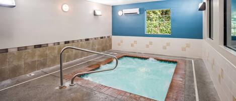 A spa area with a hot tub, tiled walls, and a window with a view of greenery.