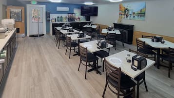 A restaurant with multiple tables and chairs, a kitchen area, and an exit sign.