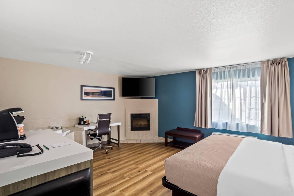 Une chambre d’hôtel équipée d’un lit, d’un bureau, d’une chaise, d’une cheminée, d’une télévision et d’une grande fenêtre avec des rideaux.