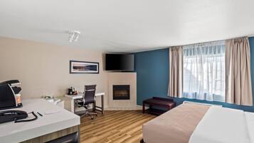 Habitación de hotel con cama, escritorio, silla, chimenea, televisor y ventana grande con cortinas.
