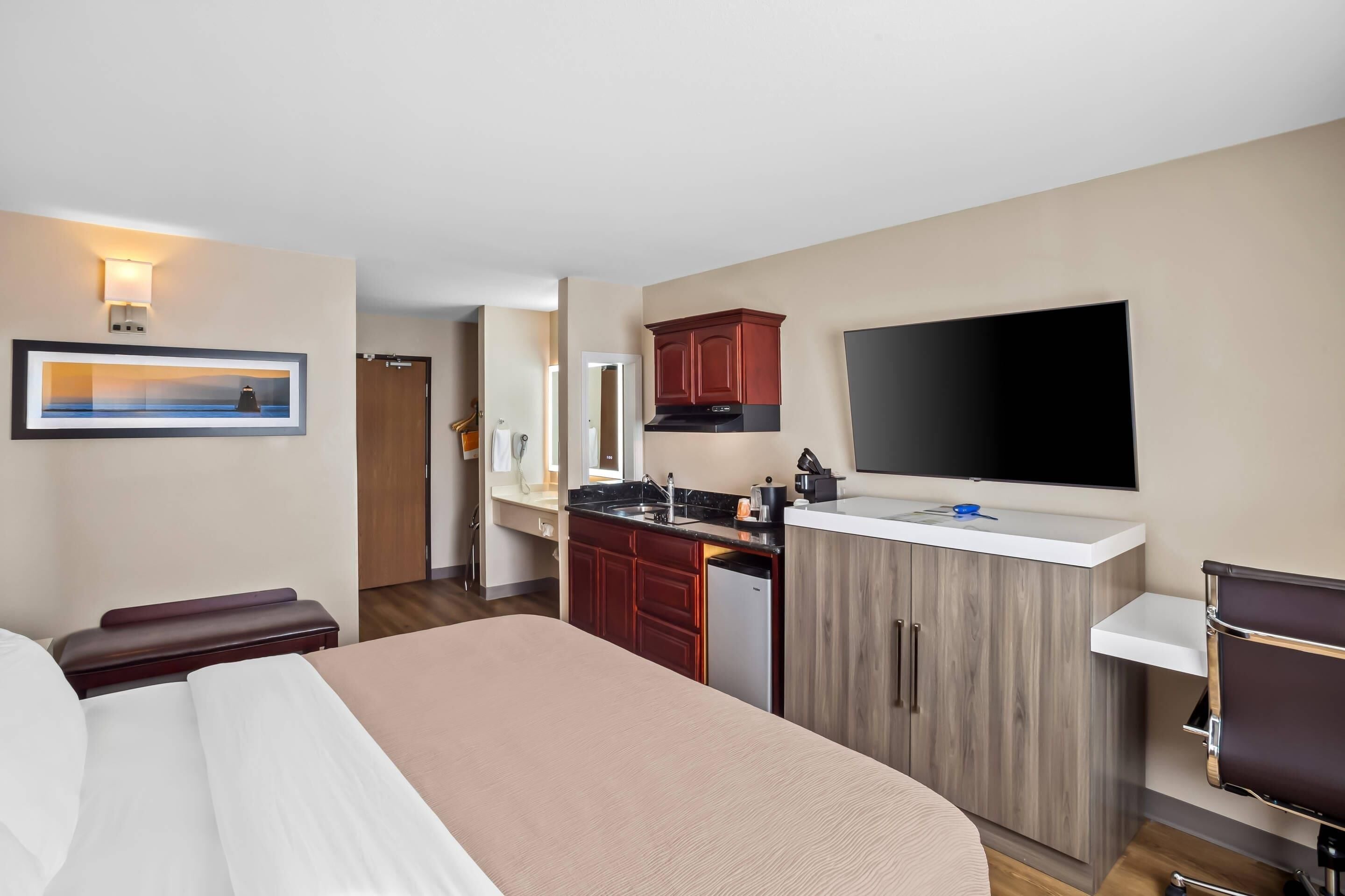 Ein Hotelzimmer mit Bett, einer kleinen Küchenzeile, einem Fernseher und einem Badezimmer.