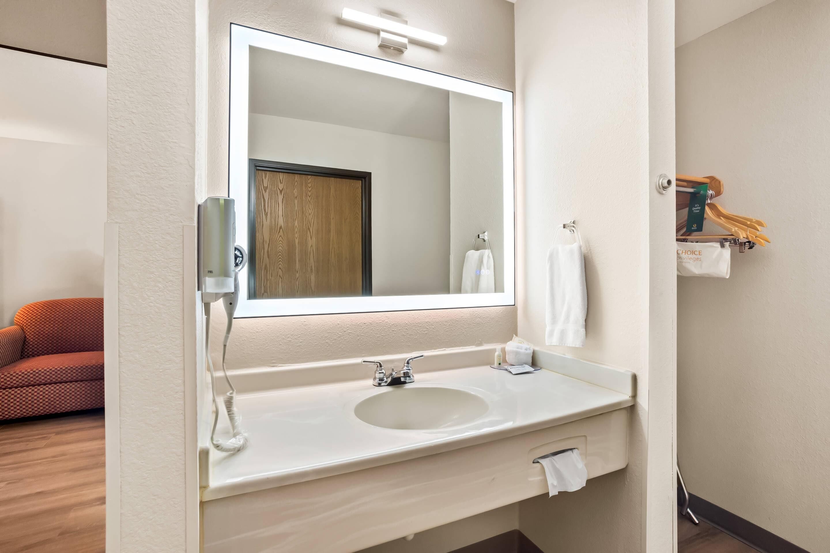 A hotel bathroom with a large mirror, a sink, and a towel rack.