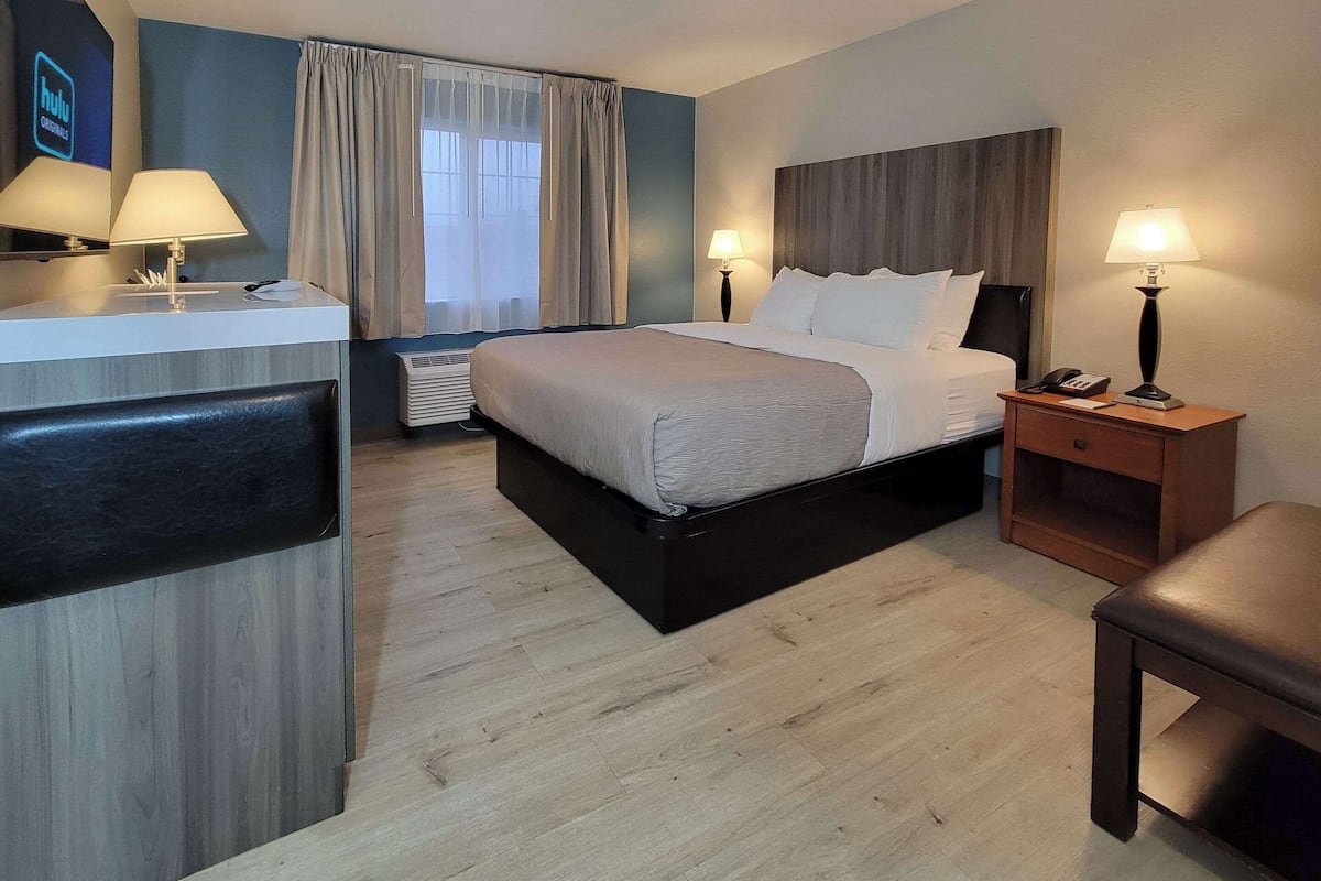 Une chambre d’hôtel avec un lit, des lampes de chevet, un bureau et une chaise.
