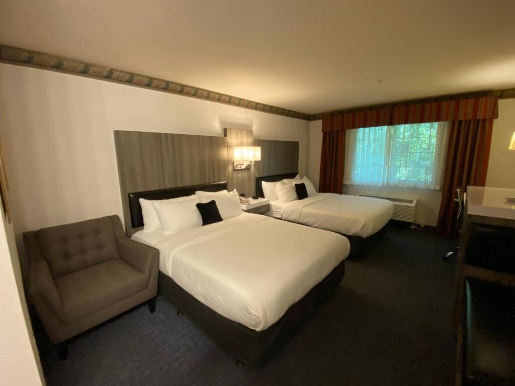 A hotel room with two beds, a sofa, a desk, and a window with curtains.