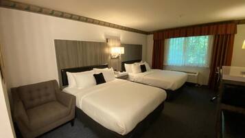 A hotel room with two beds, a sofa, a desk, and a window with curtains.