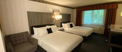 Habitación de hotel con dos camas, un sofá, un escritorio y un ventanal con cortinas.