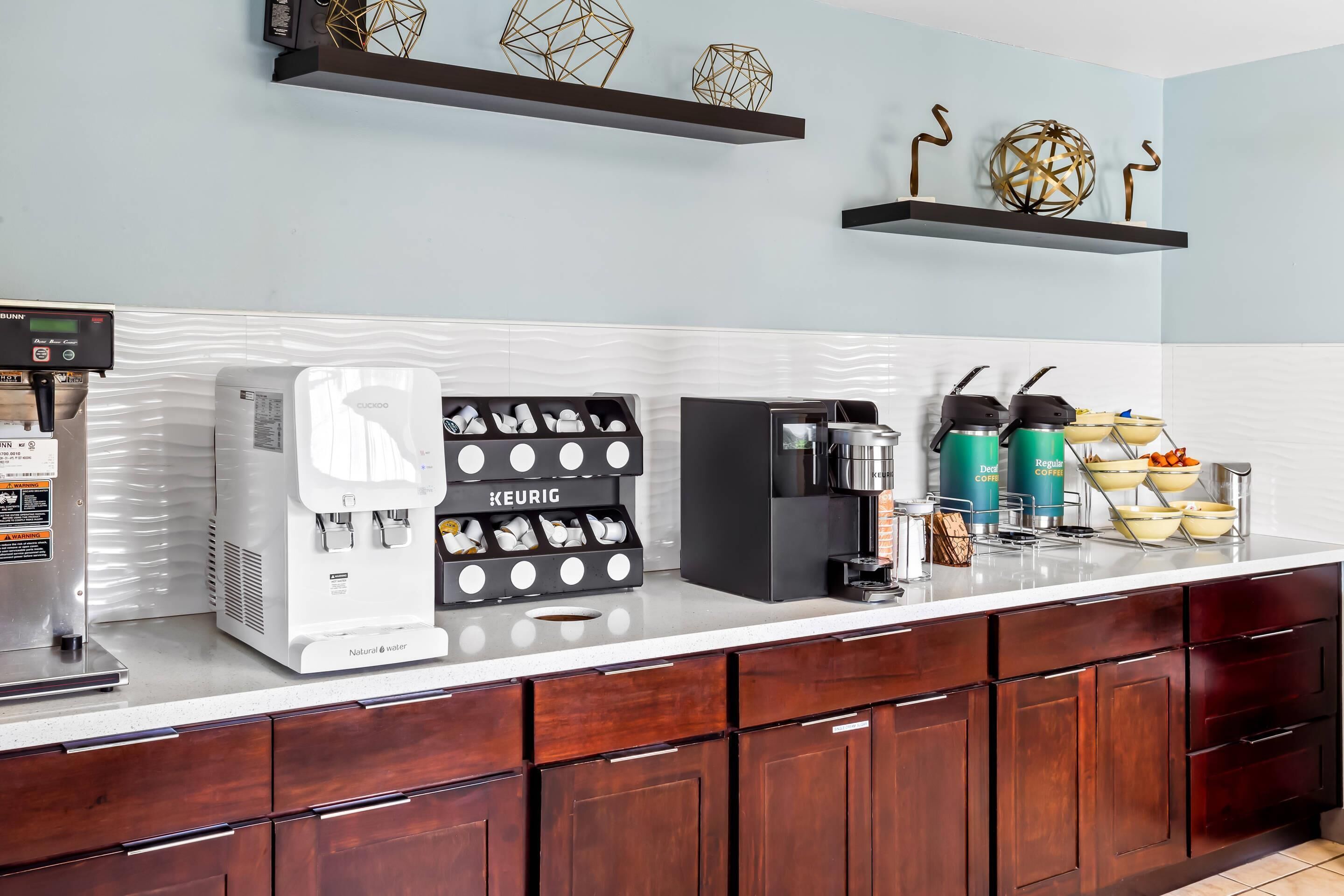 A modern kitchen with a coffee station, including a Keurig coffee maker, a water dispenser, and a coffee machine.
