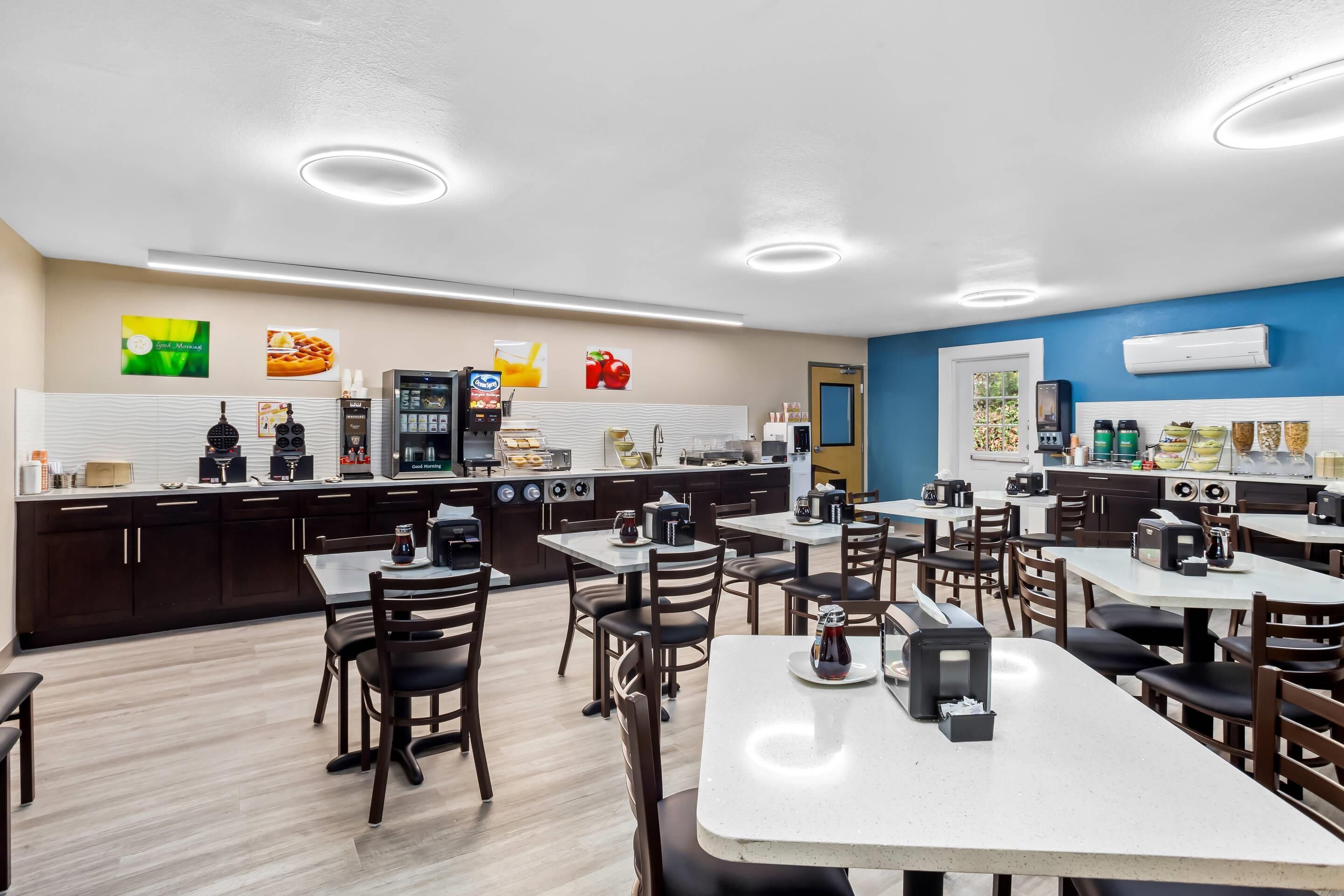 A modern kitchen and dining area with dark wooden cabinets, white countertops, and a variety of appliances including a coffee machine and a microwave.