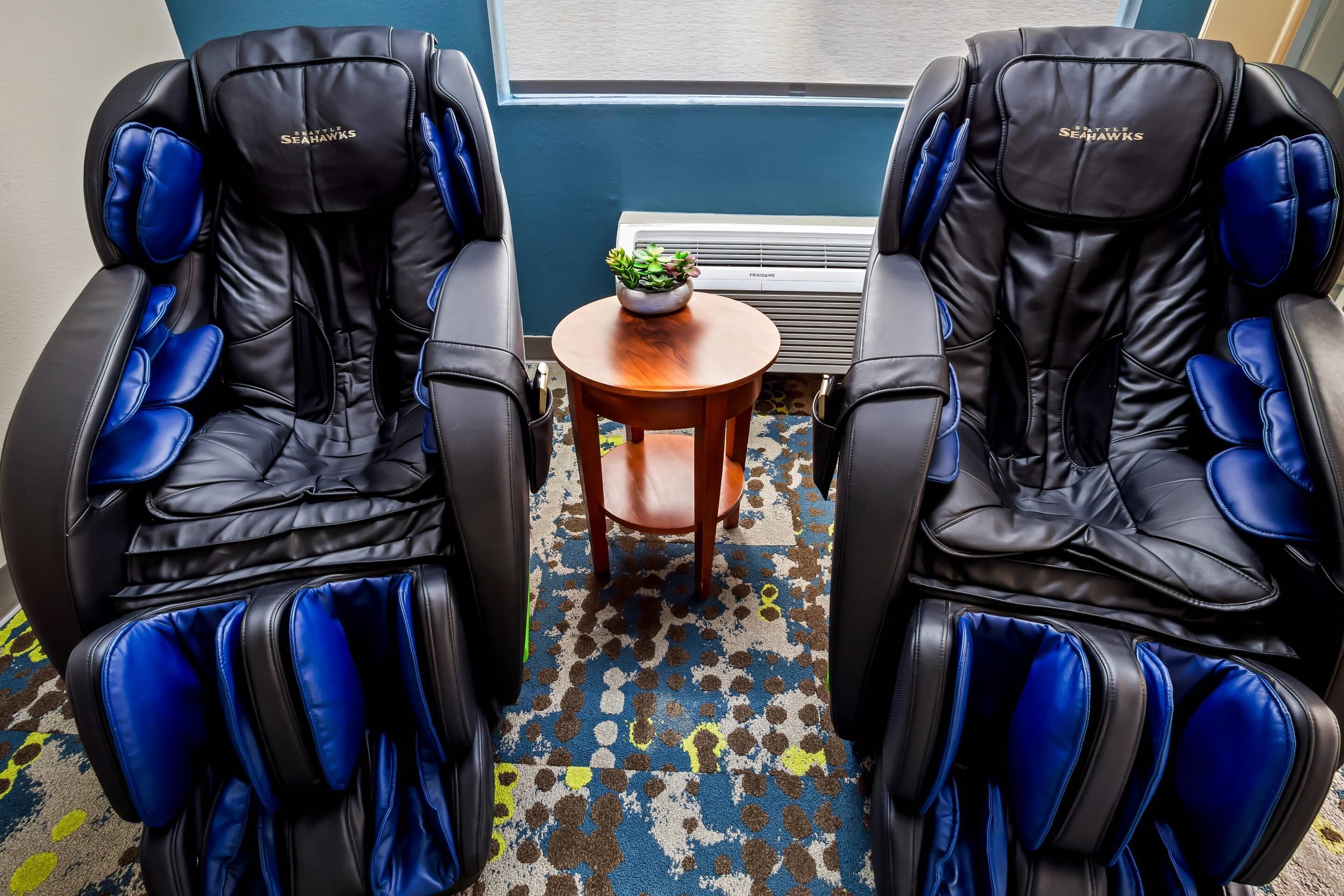 Deux fauteuils de massage aux accents bleus, une petite table en bois avec une plante et un tapis à motifs.