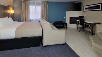 A hotel room with a bed, a sofa, a desk, a chair, a TV, and a fireplace.