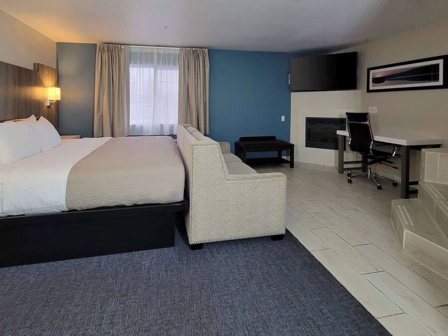 A hotel room with a bed, a sofa, a desk, a chair, a TV, and a fireplace.
