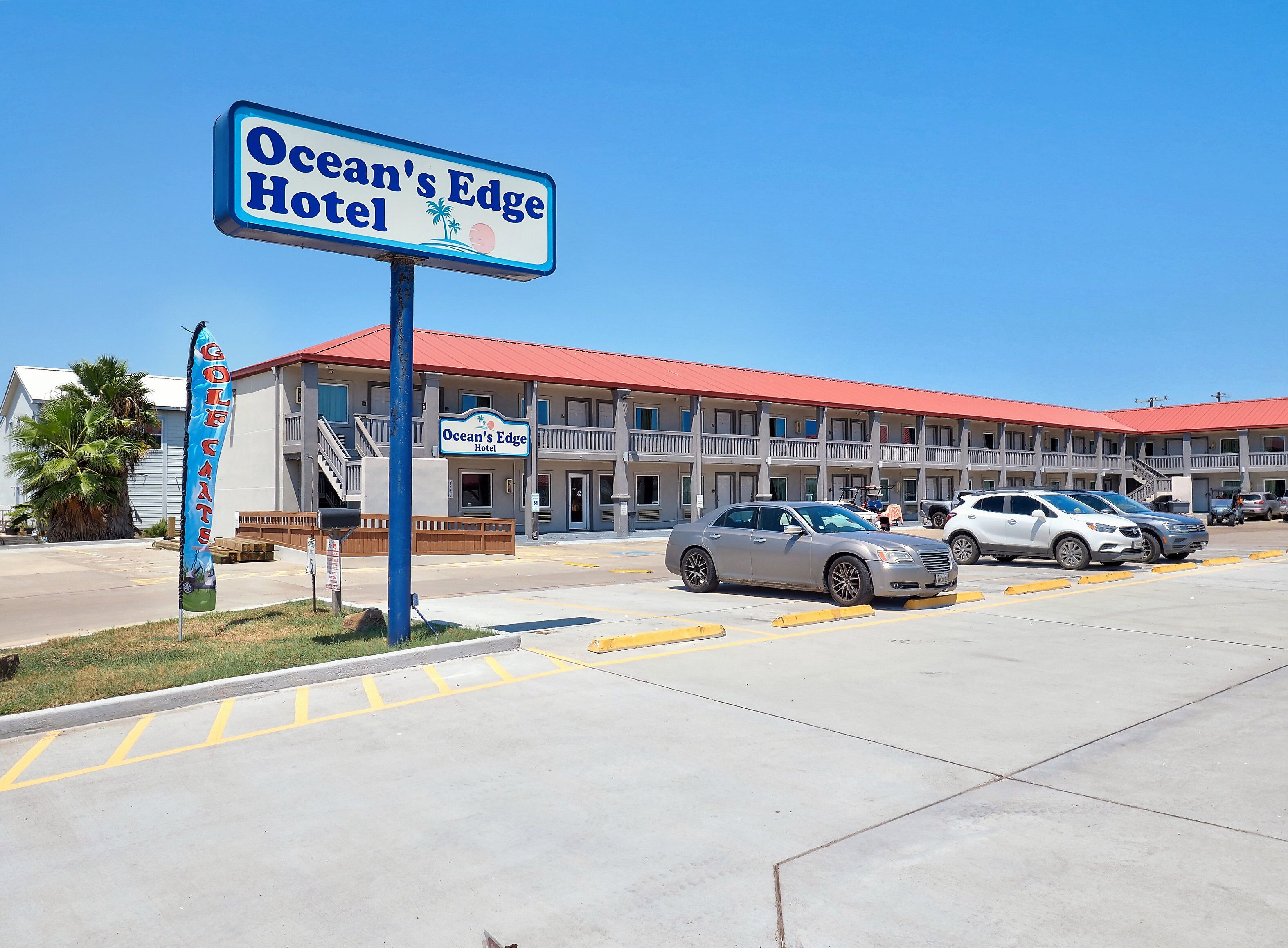 Ocean's Edge Hotel with a red roof, multiple balconies, and a parking lot with several cars.