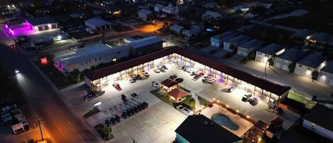 An aerial view of a commercial area with a well-lit parking lot, a gas station, and various buildings.