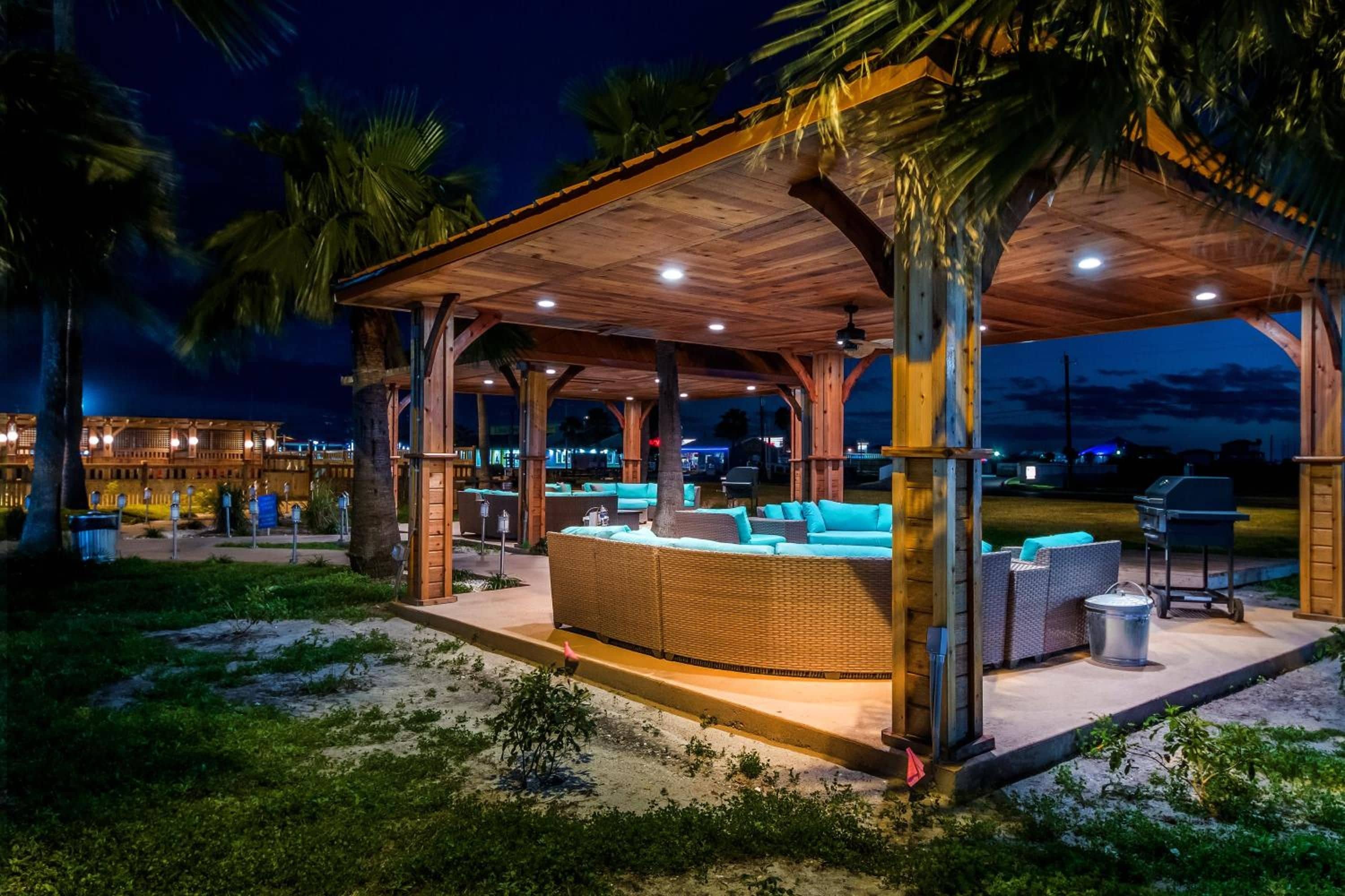 Un espacio de estar techado al aire libre con mobiliario de mimbre y una parrilla.