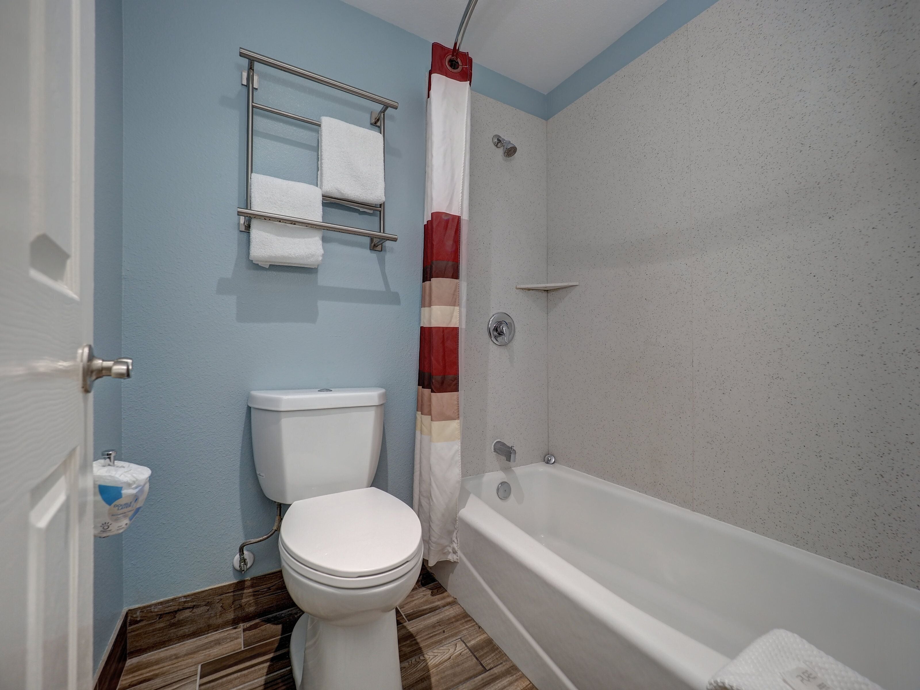A bathroom with a toilet, a shower with a curtain, and a towel rack with towels.